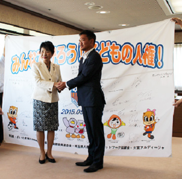 上川法務大臣と大宮アルディージャのアンバサダー塚本泰史さんが握手する様子