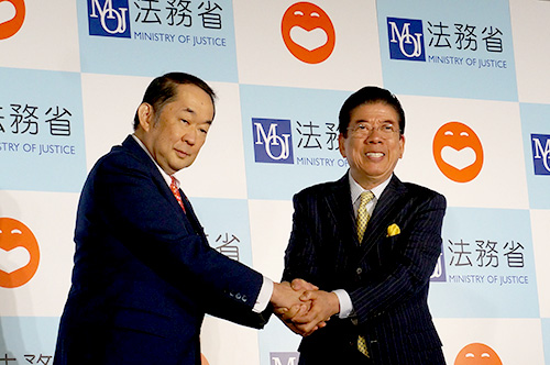金田法務大臣（当時）と西川きよしさんが登壇し，固い握手を交わしたときの様子