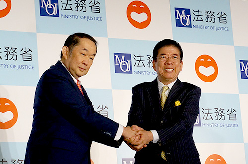 金田法務大臣(当時)と西川きよしさんが登壇し,固い握手を交わしたときの様子