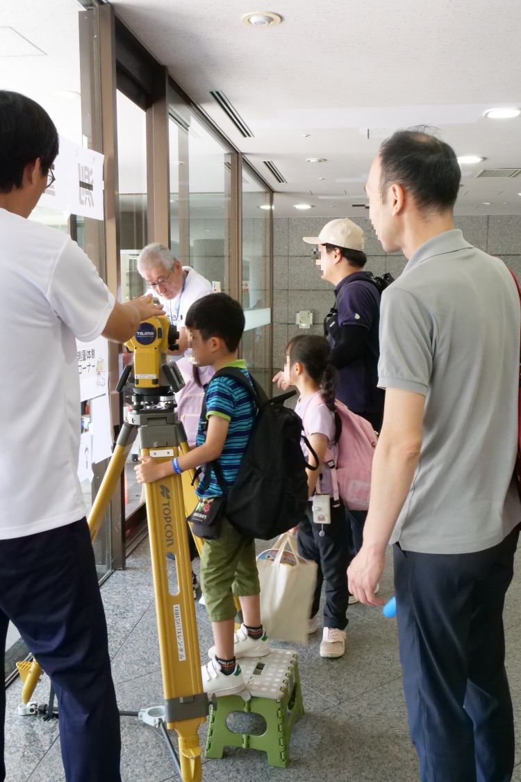 「土地家屋調査士の仕事を勉強しよう!」のコーナーでは、トータルステーションを覗いて測量体験をしていただきました。