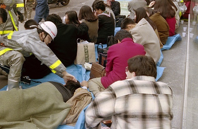 地下鉄日比谷線の小伝馬町駅から地上に出て倒れたサリン中毒症の乗客を手当てする救急隊員（平成7年3月20日、写真：毎日新聞社/アフロ）